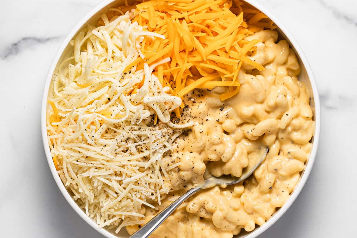 White bowl filled with mac and cheese and shredded cheese