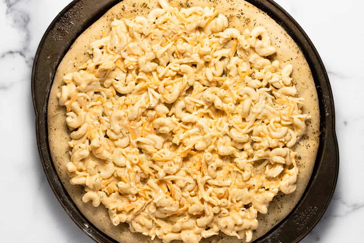 Pizza crust on a pizza pan topped with macaroni and cheese