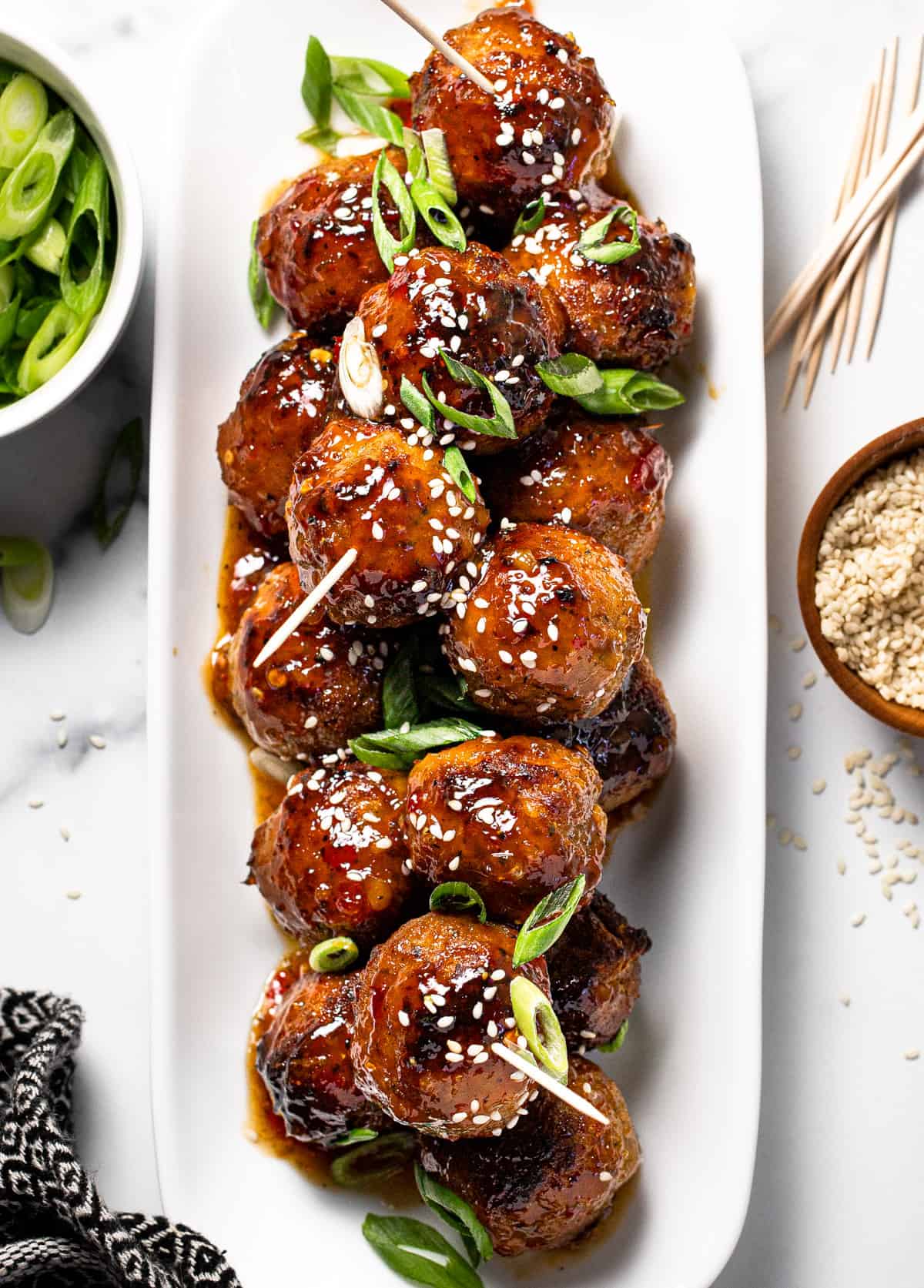White platter filled with glazed meatballs garnished with green onion