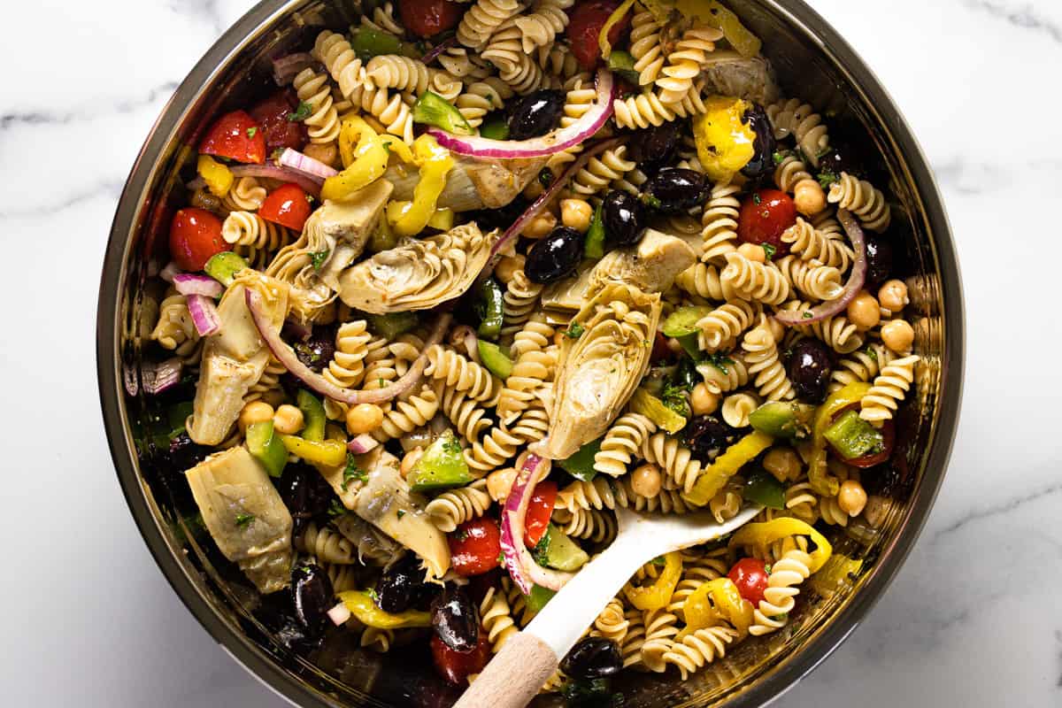 Large metal bowl filled with ingredients to make vegan pasta salad