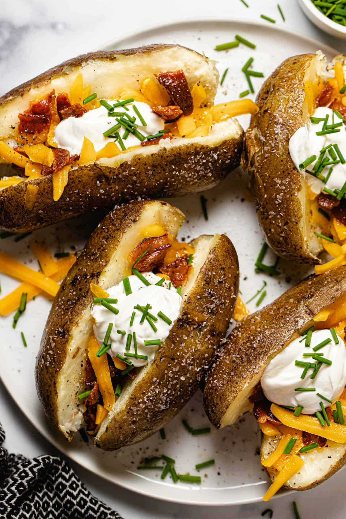 White plate with four loaded baked potatoes garnished with chives