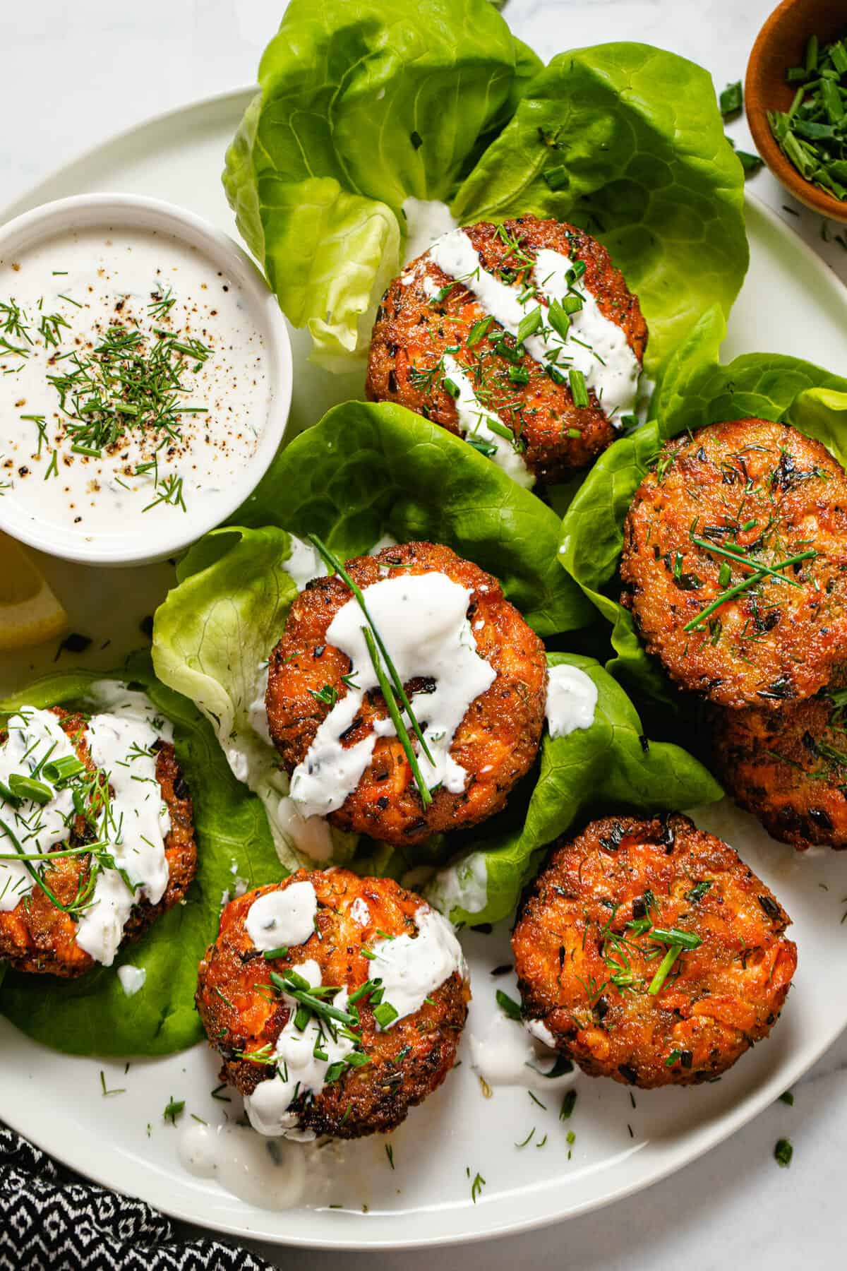 White plate with salmon patties wrapped in lettuce drizzled with tzatziki