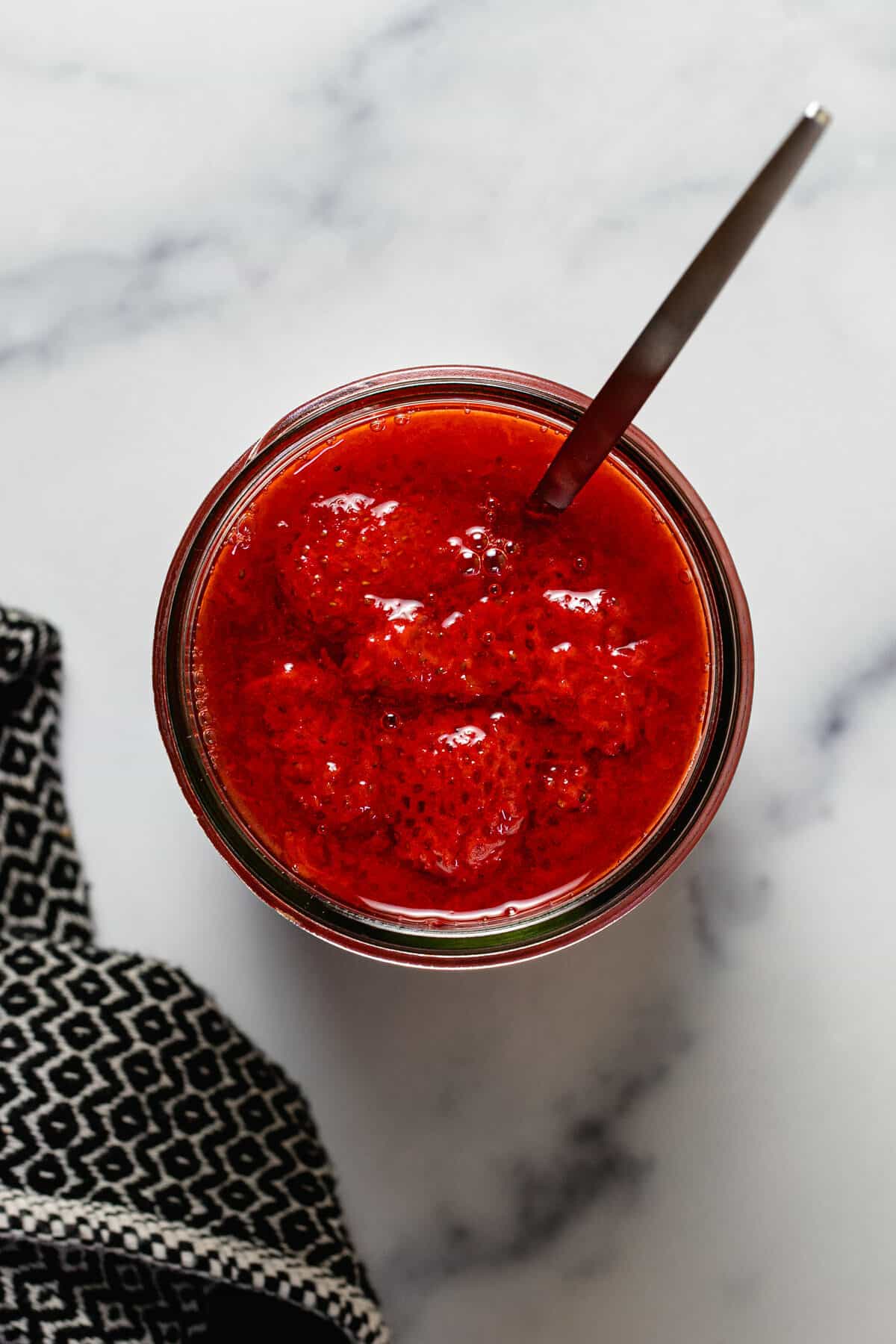 Overhead shot of a wide mouth mason jar filled with strawberry sauce