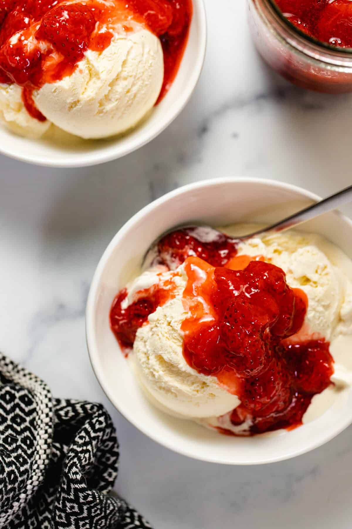 Overhead shot of two bowls of vanilla ice cream topped with strawberry compote