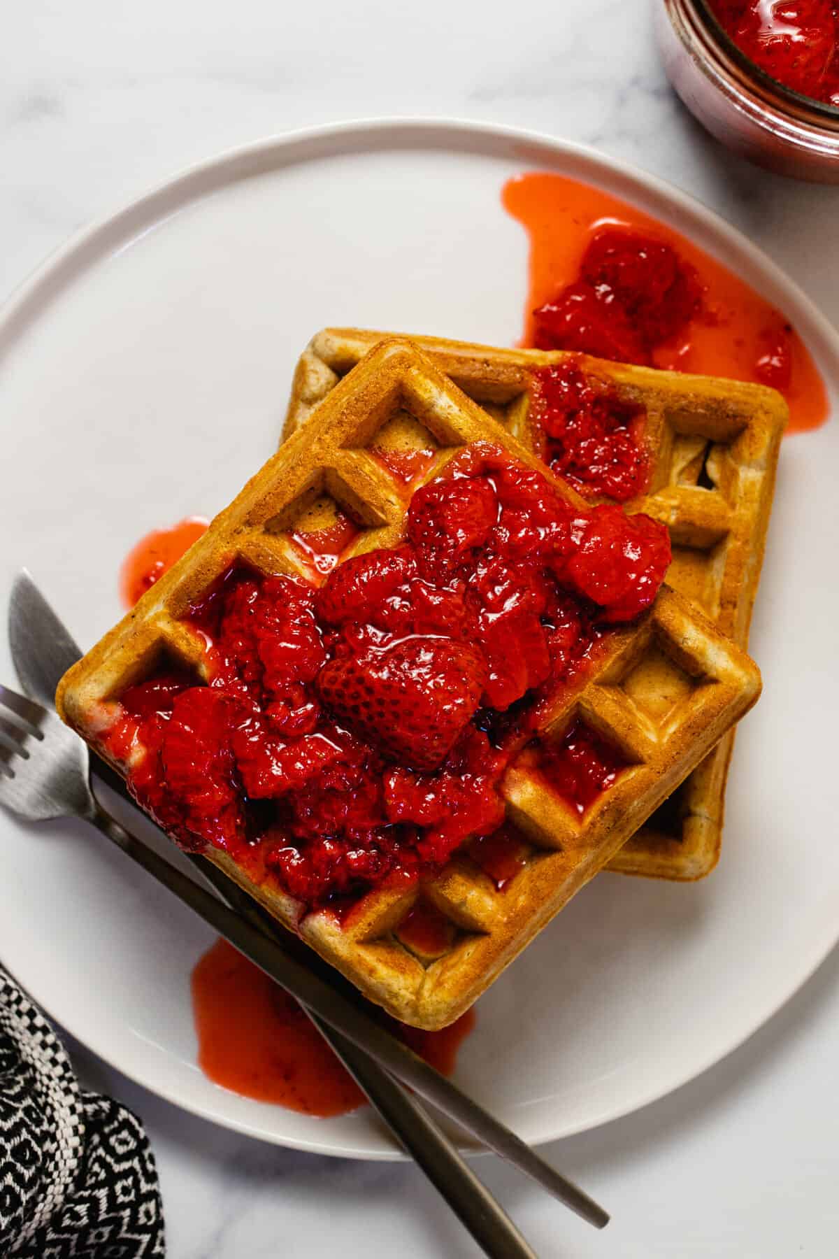 Two waffles drizzled with strawberry compote on a white plate