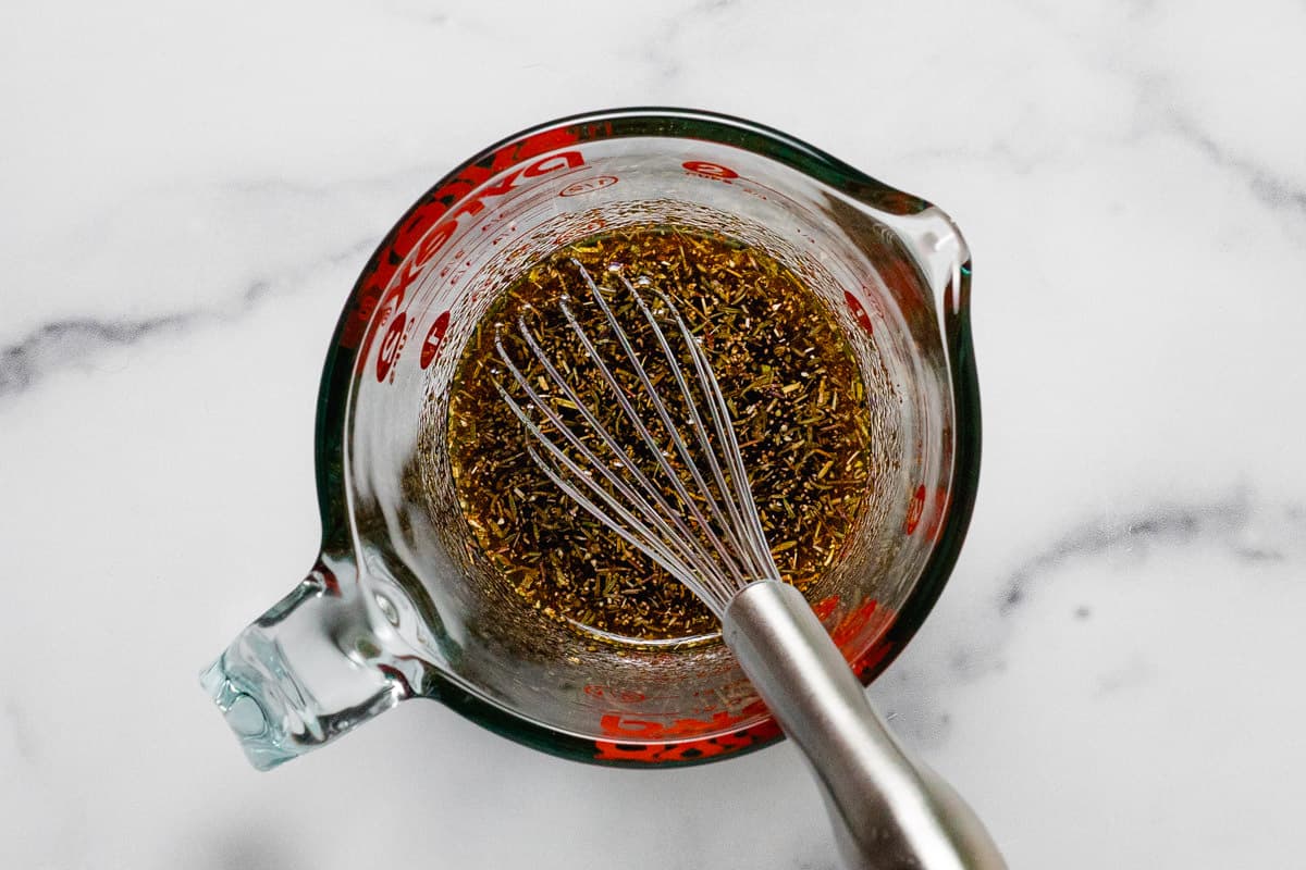 Measuring cup filled with olive oil herbs and spices for homemade fries