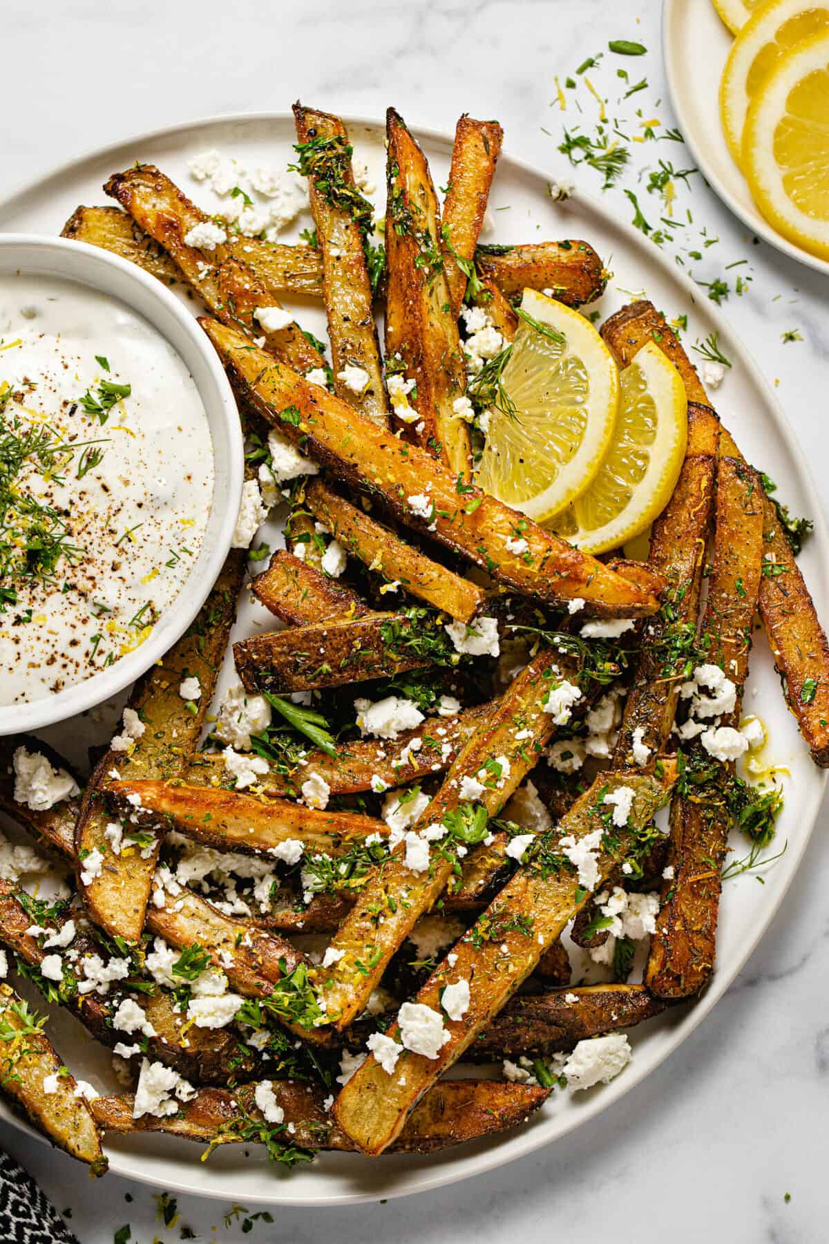 Large white plate filled with homemade Greek fries and a bowl of dill yogurt sauce