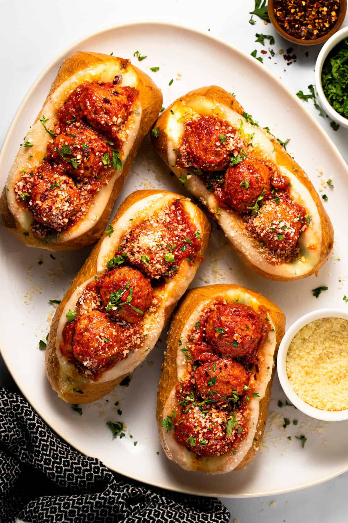 Meatball subs garnished with parsley on a large white serving platter
