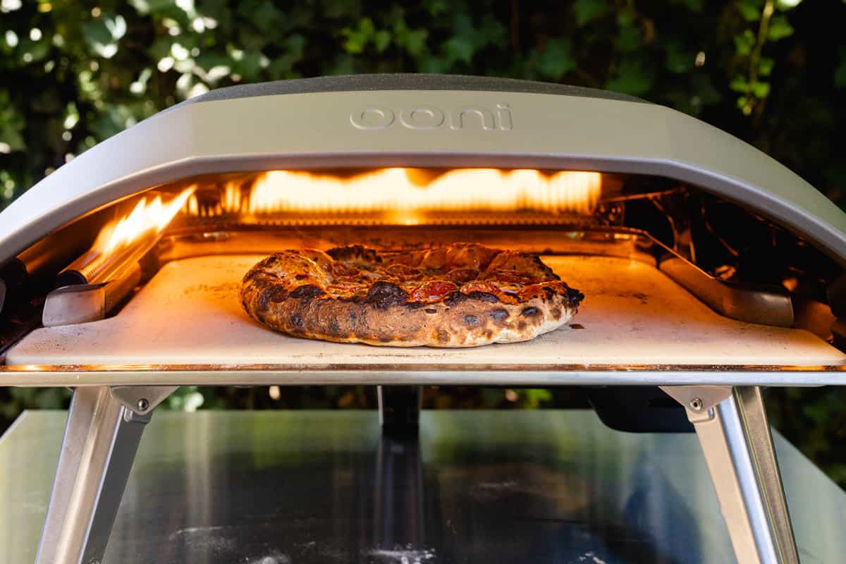 A small pizza cooking inside an Ooni pizza oven outside