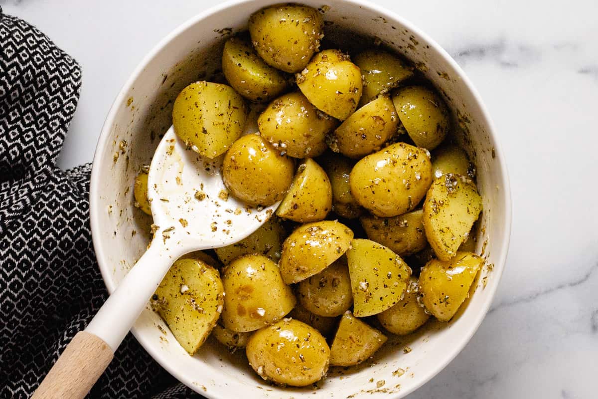 Boiled potatoes in a large white bowl tossed with olive oil and dried herbs