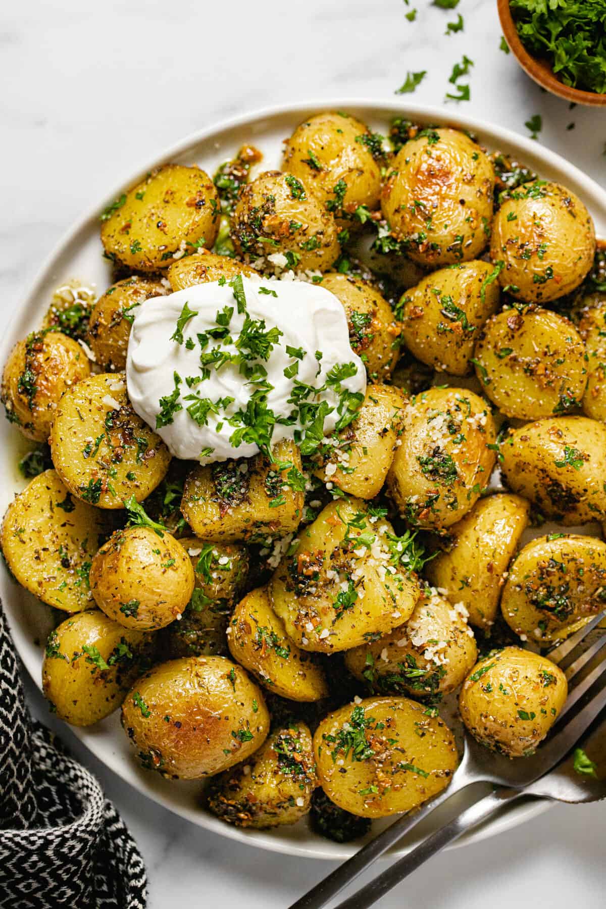 White plate filled with herby roasted baby potatoes garnished with sour cream and parsley