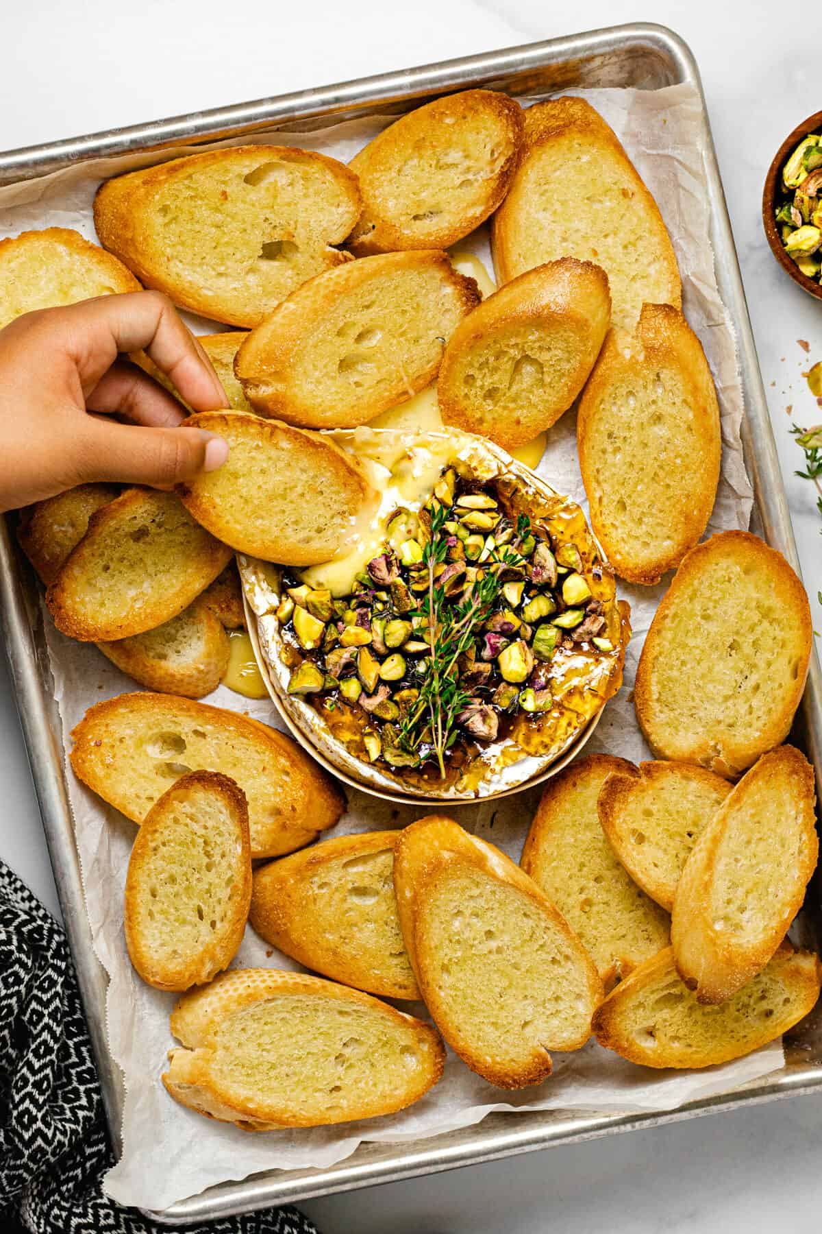 A small hand dipping a crostini into baked brie with fig jam