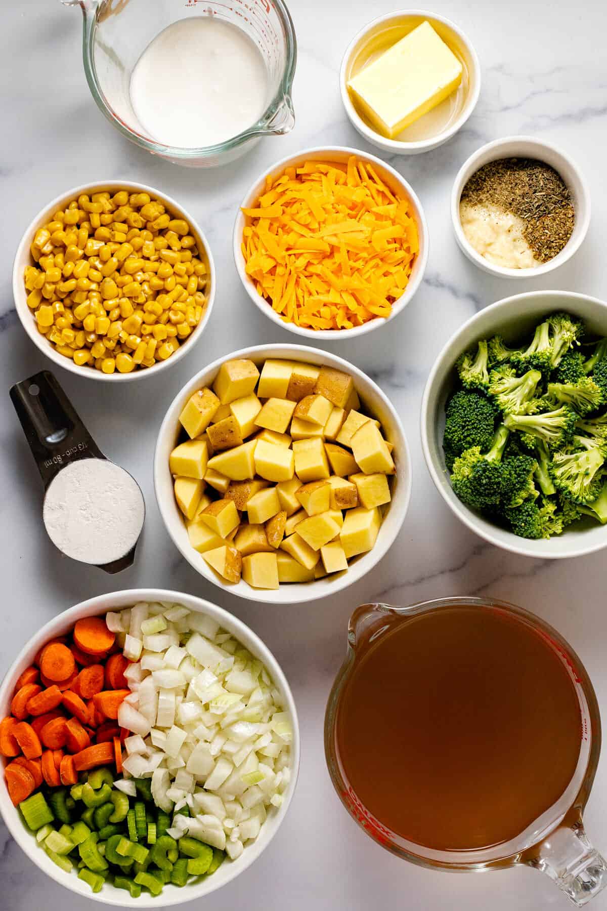 White marble counter top with bowls of ingredients to make cheesy veggie soup