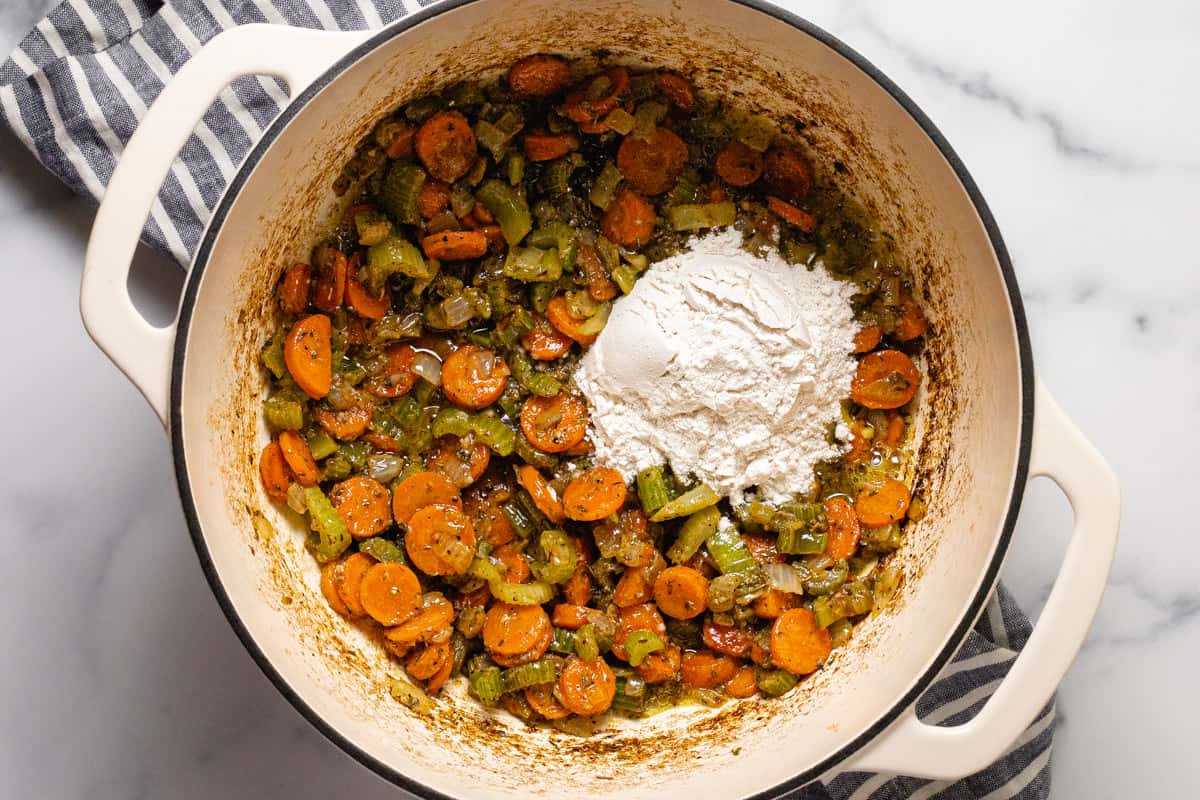 Large white pot filled with sautéed veggies a big scoop of flour