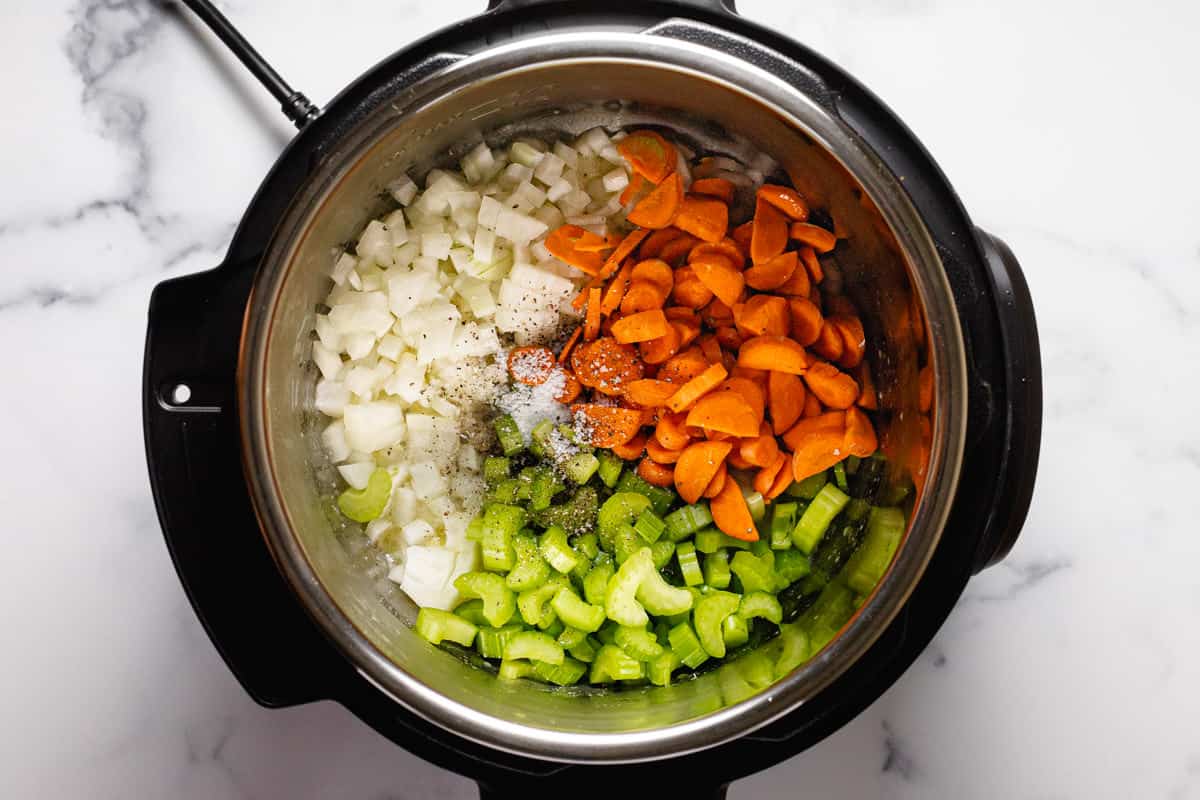 Instant pot filled with carrot onion and celery in olive oil