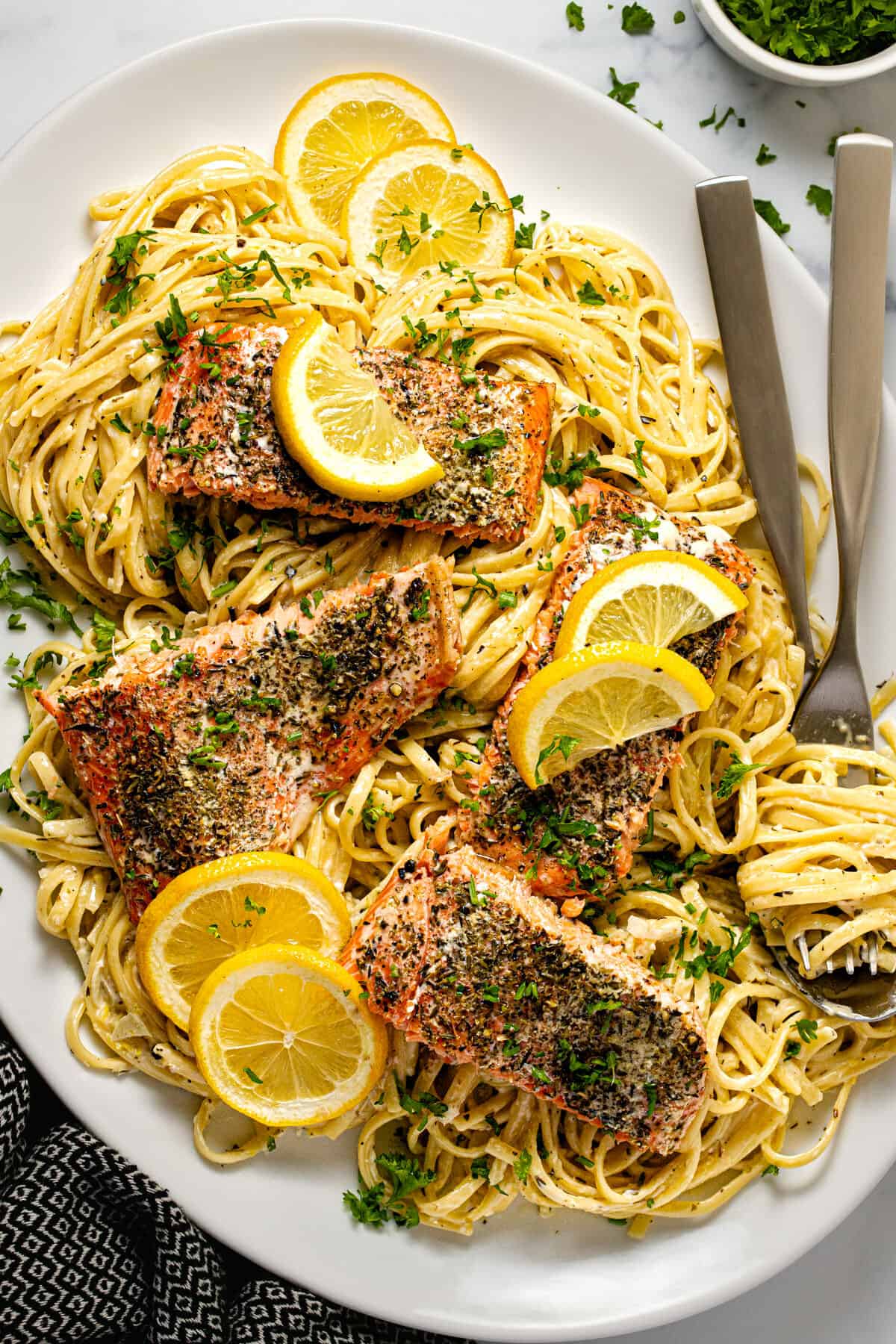 Large white serving platter filled with creamy salmon pasta garnished with parsley and lemon slices.