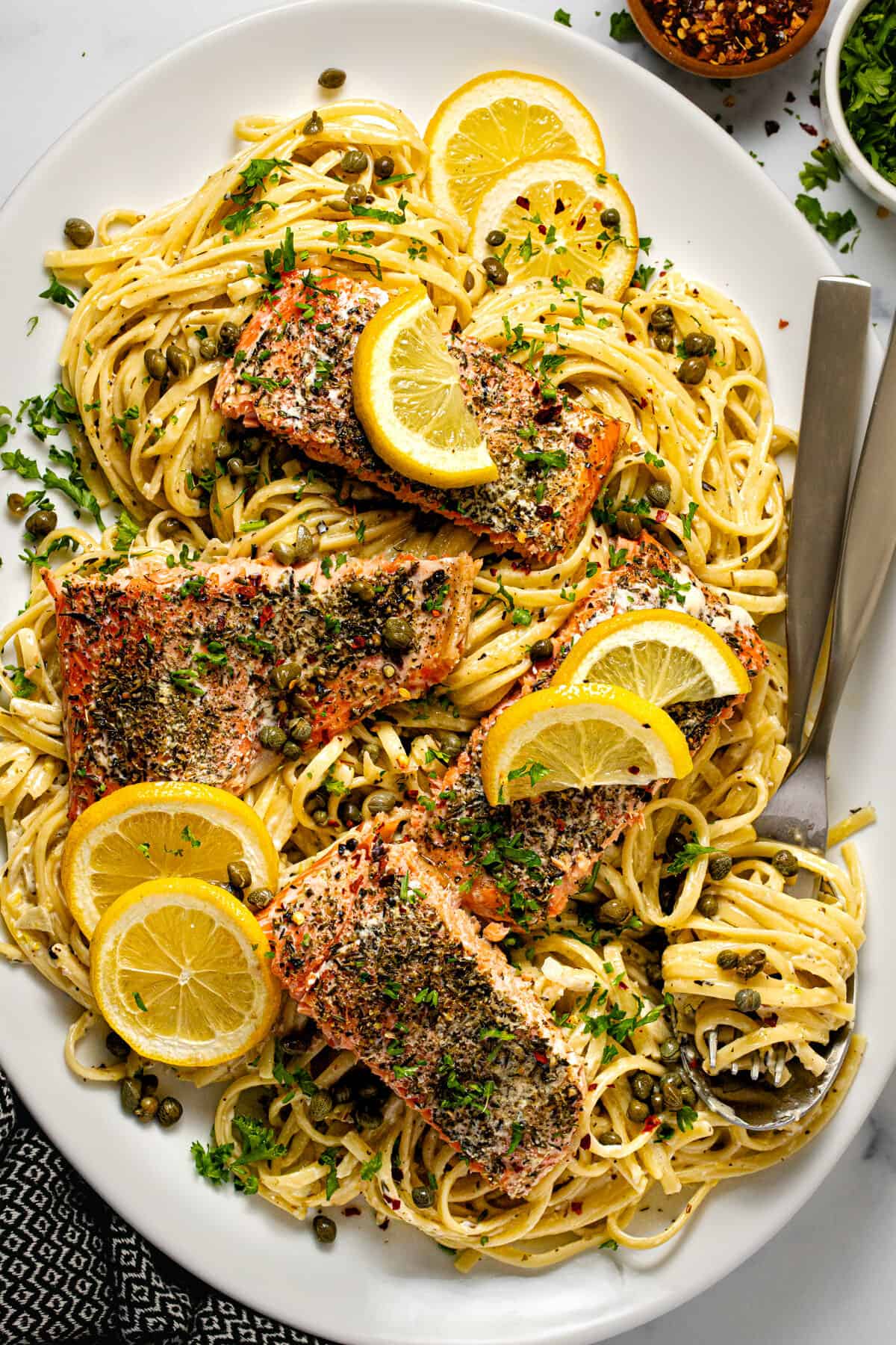White platter filled with salmon linguine in a garlic herb sauce garnished with parsley.