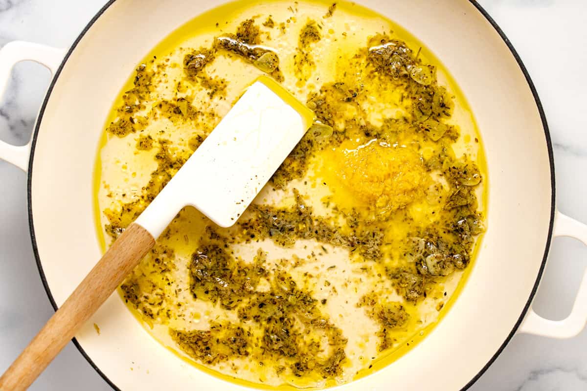 Large white sauté pan filled with garlic, herbs, lemon juice, and elmon zest.
