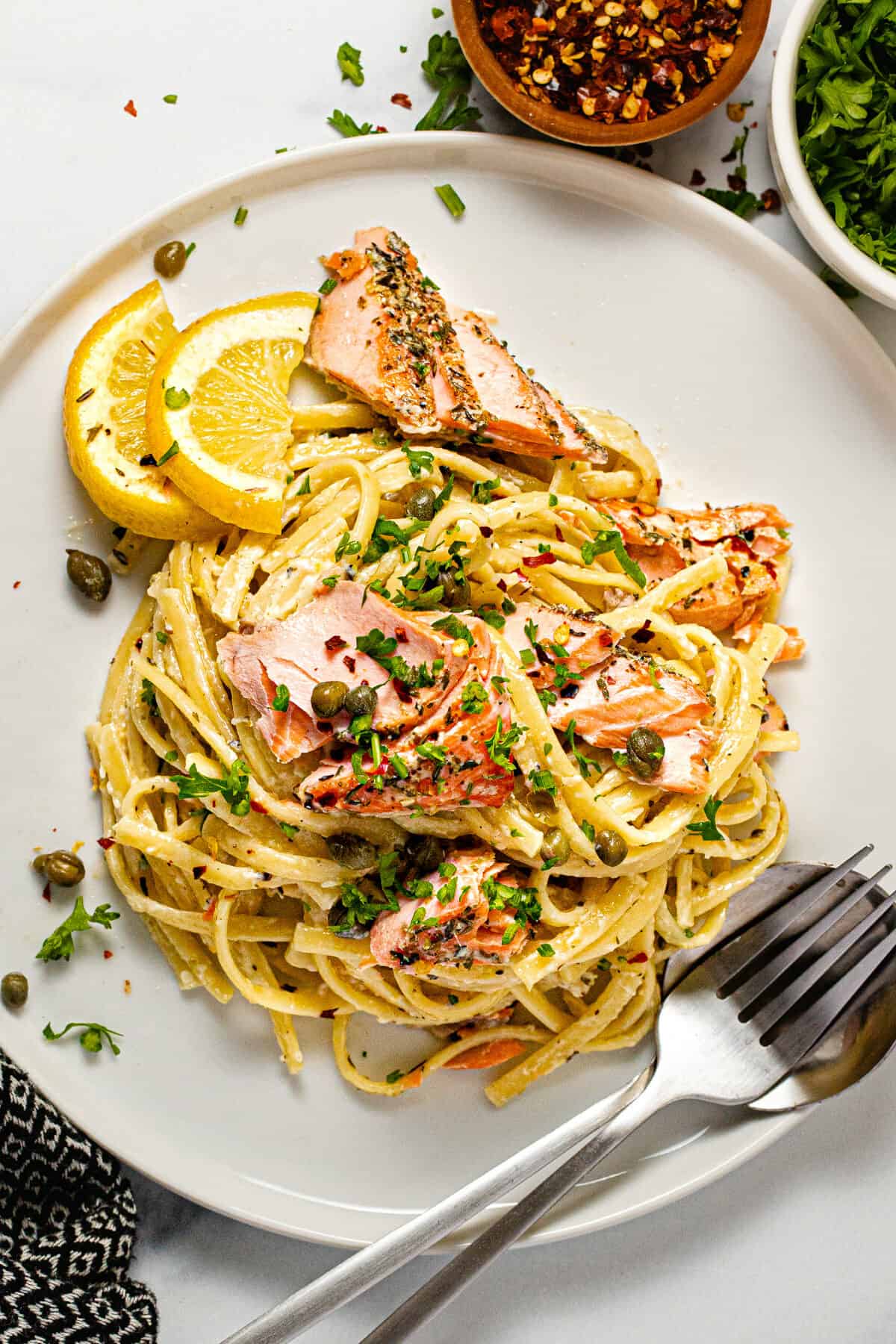 White plate filled with creamy garlic linguine and flaked salmon garnished with parsley.