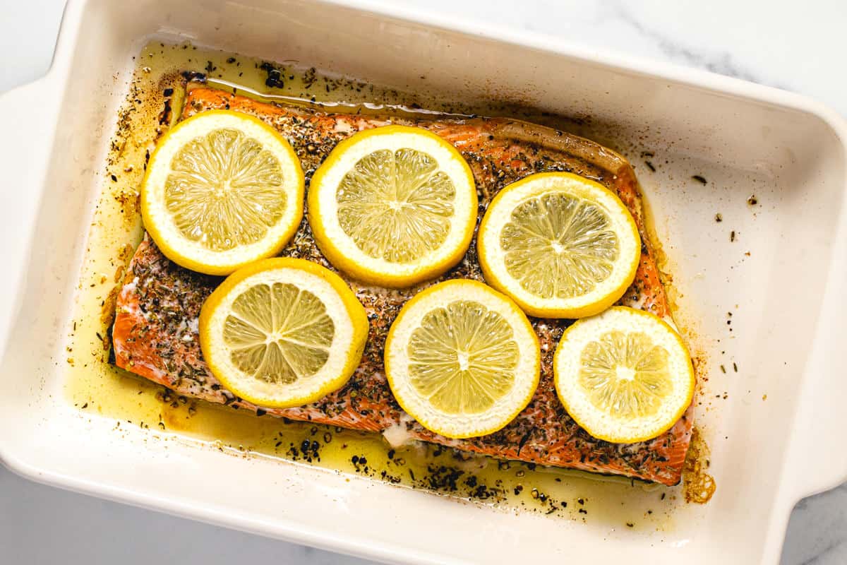 Freshly baked salmon in a white baking dish topped with sliced lemons.