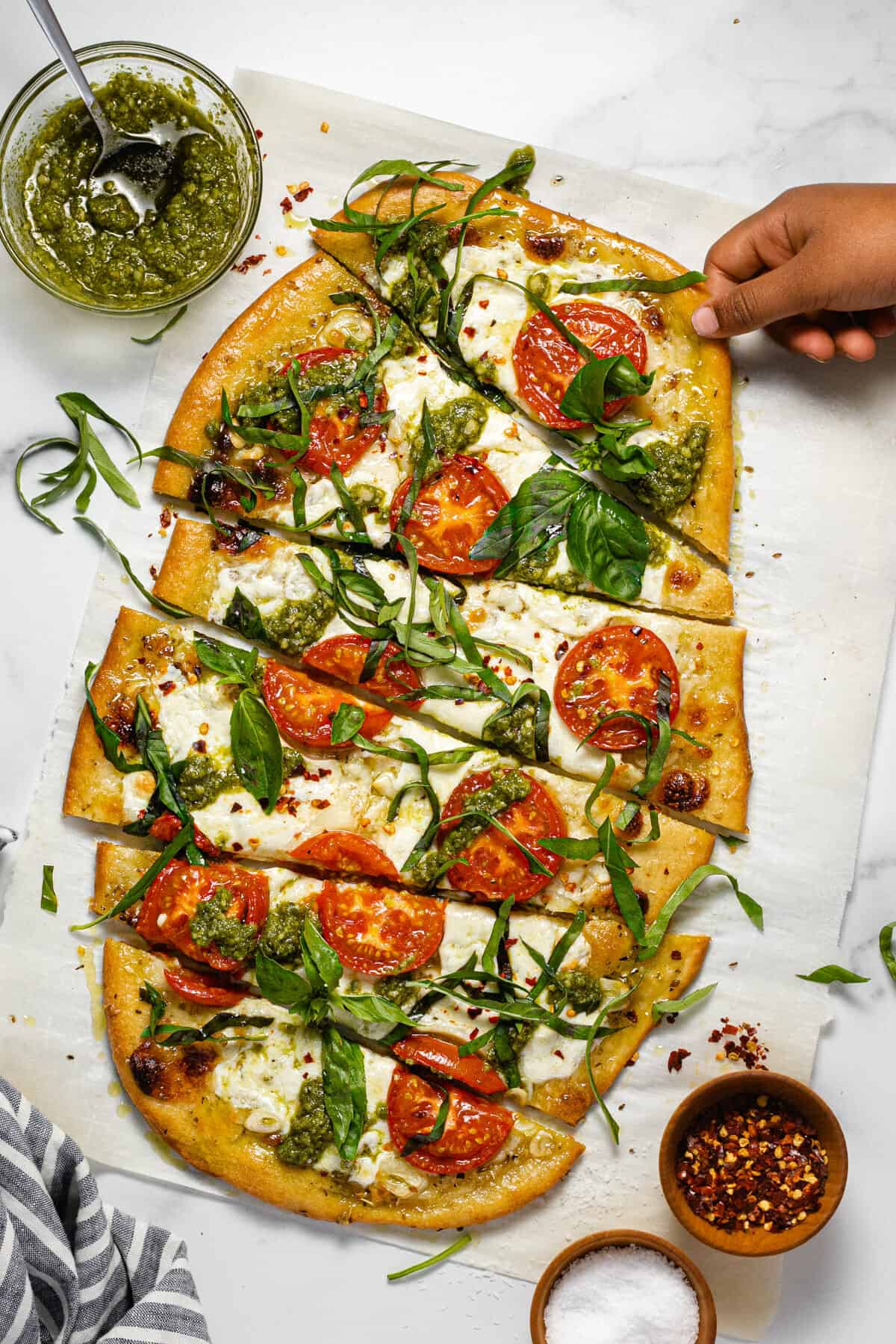 Overhead shot of a small hand reaching for a slice of Margherita flatbread garnished with fresh basil