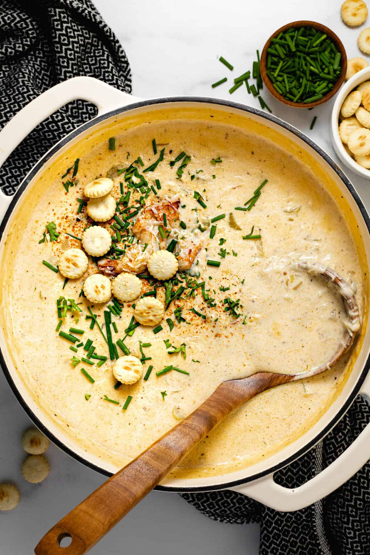 White pot filled with creamy homemade crab chowder garnished with crackers and chives