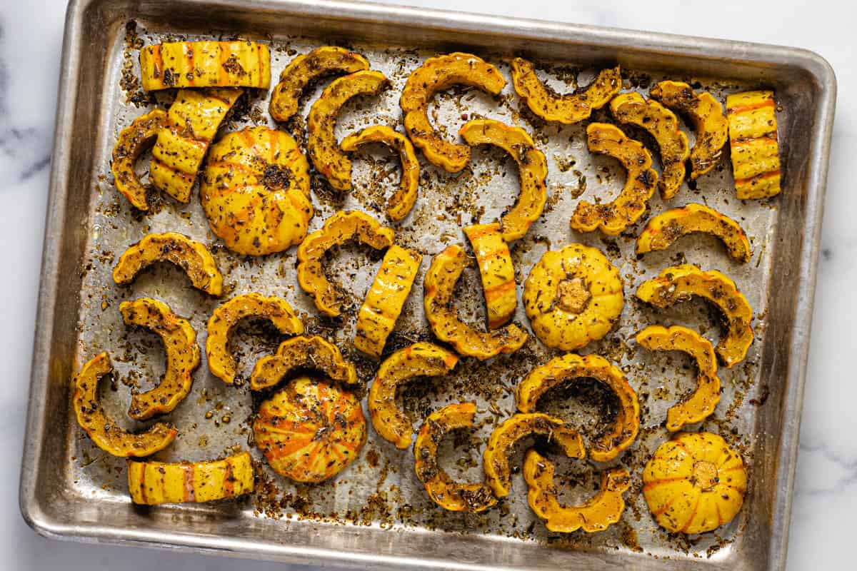 Sliced herb roasted delicata squash on a small metal baking sheet