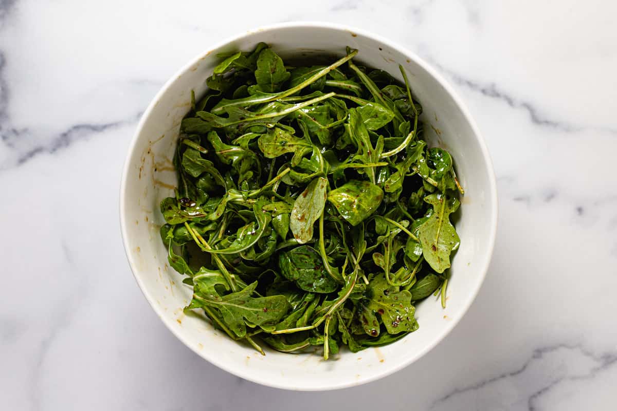 Large white bowl filled with spring greens tossed in olive oil and balsamic vinegar