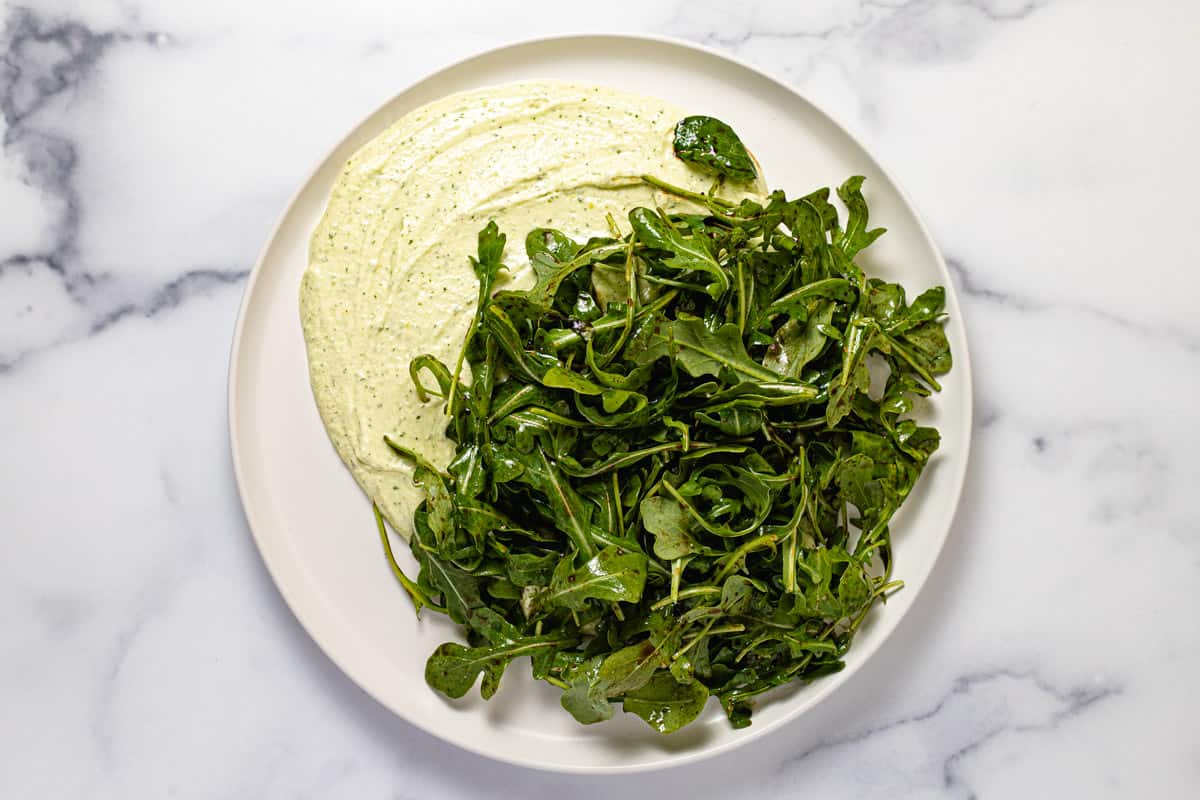 White plate with a large dollop of creamy whipped feta dip topped with dressed spring greens