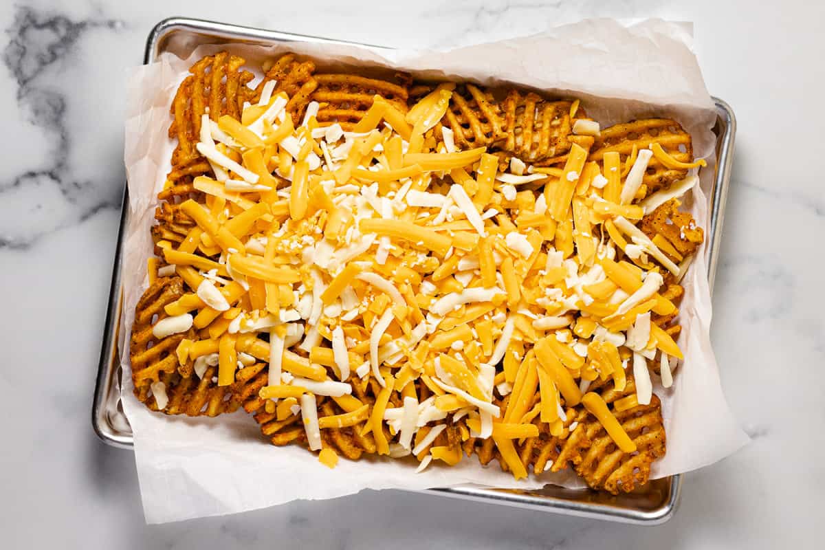 Baking sheet with waffles fries and shredded cheese