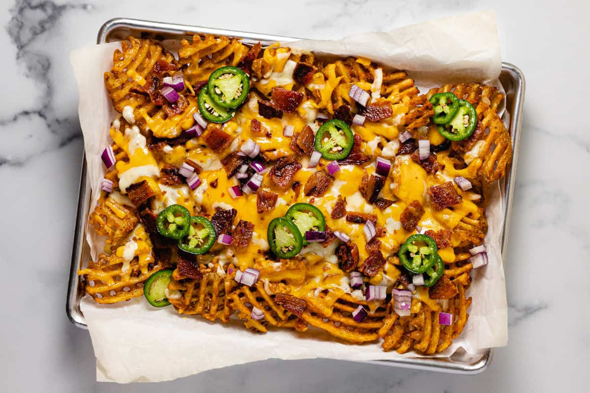 Baking sheet with waffle fries topped with cheese and bacon