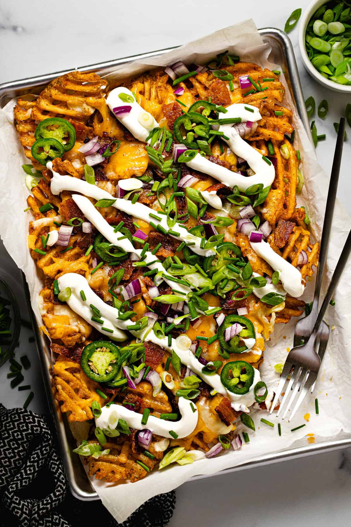 Small baking sheet filled with loaded fries garnished with sour cream and green onion