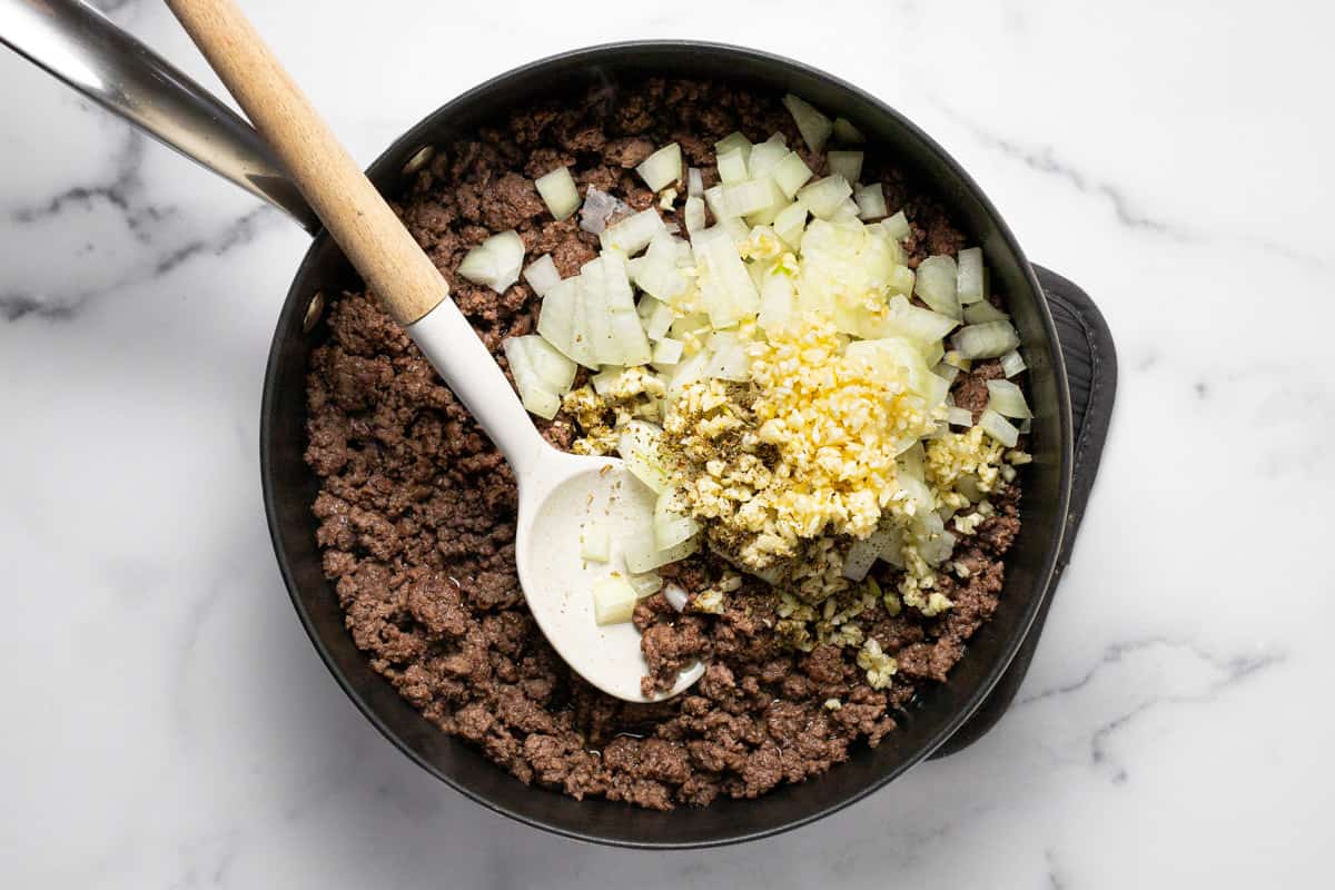 Large sauté pan filled with ground beef diced onion and minced garlic