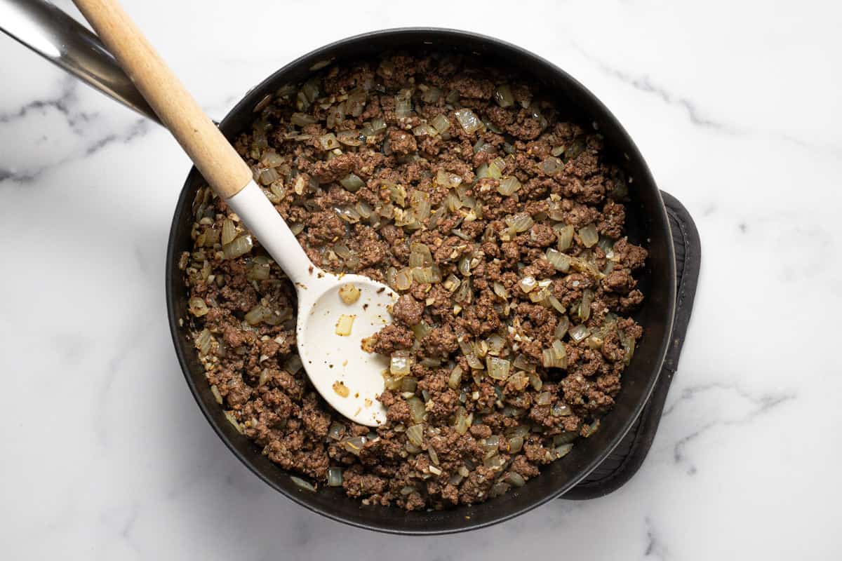 Large sauté pan filled with ground beef diced onion and minced garlic