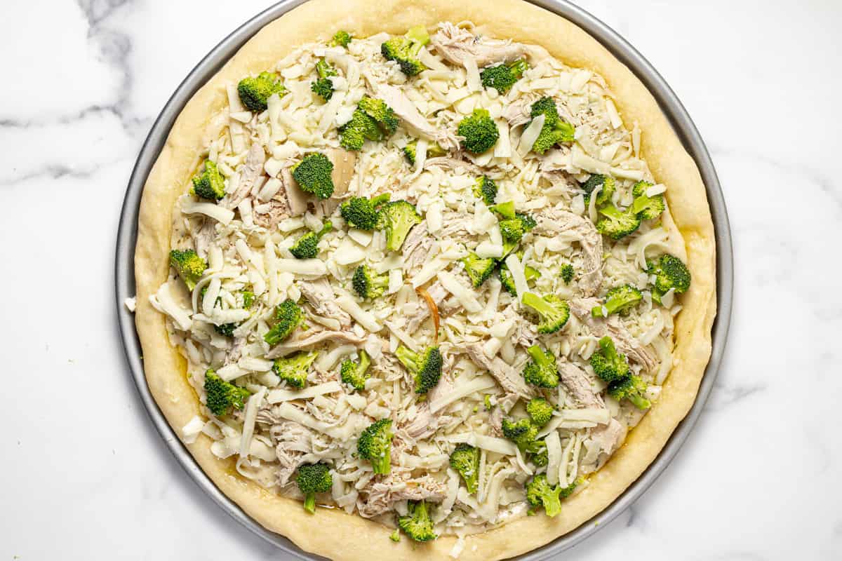 Pizza crust topped with ingredients to make chicken alfredo pizza
