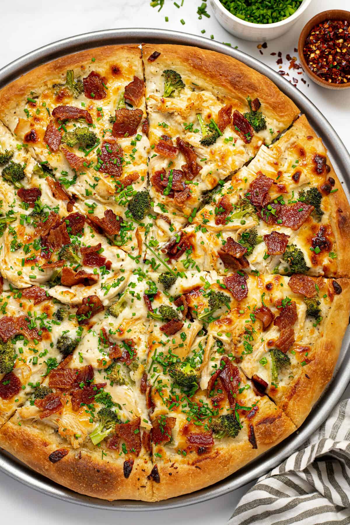 Overhead shot of a chicken alfredo pizza garnished with sliced chives