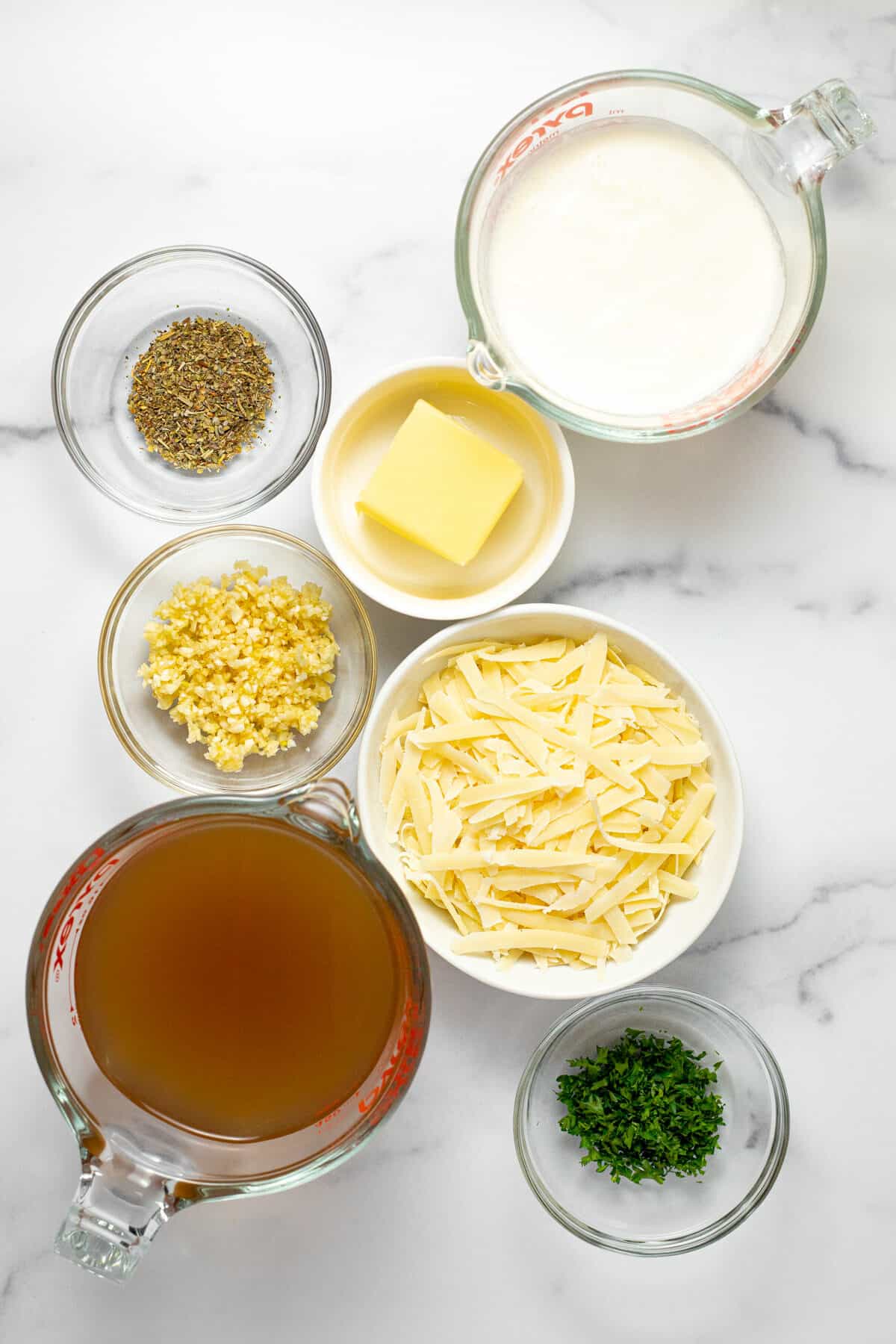 White marble counter top with bowls of ingredients to make Parmesan garlic sauce
