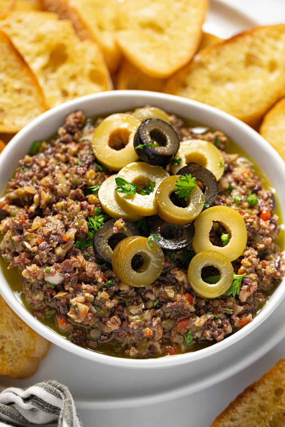 White bowl filled with homemade olive tapenade garnished with sliced olives and parsley