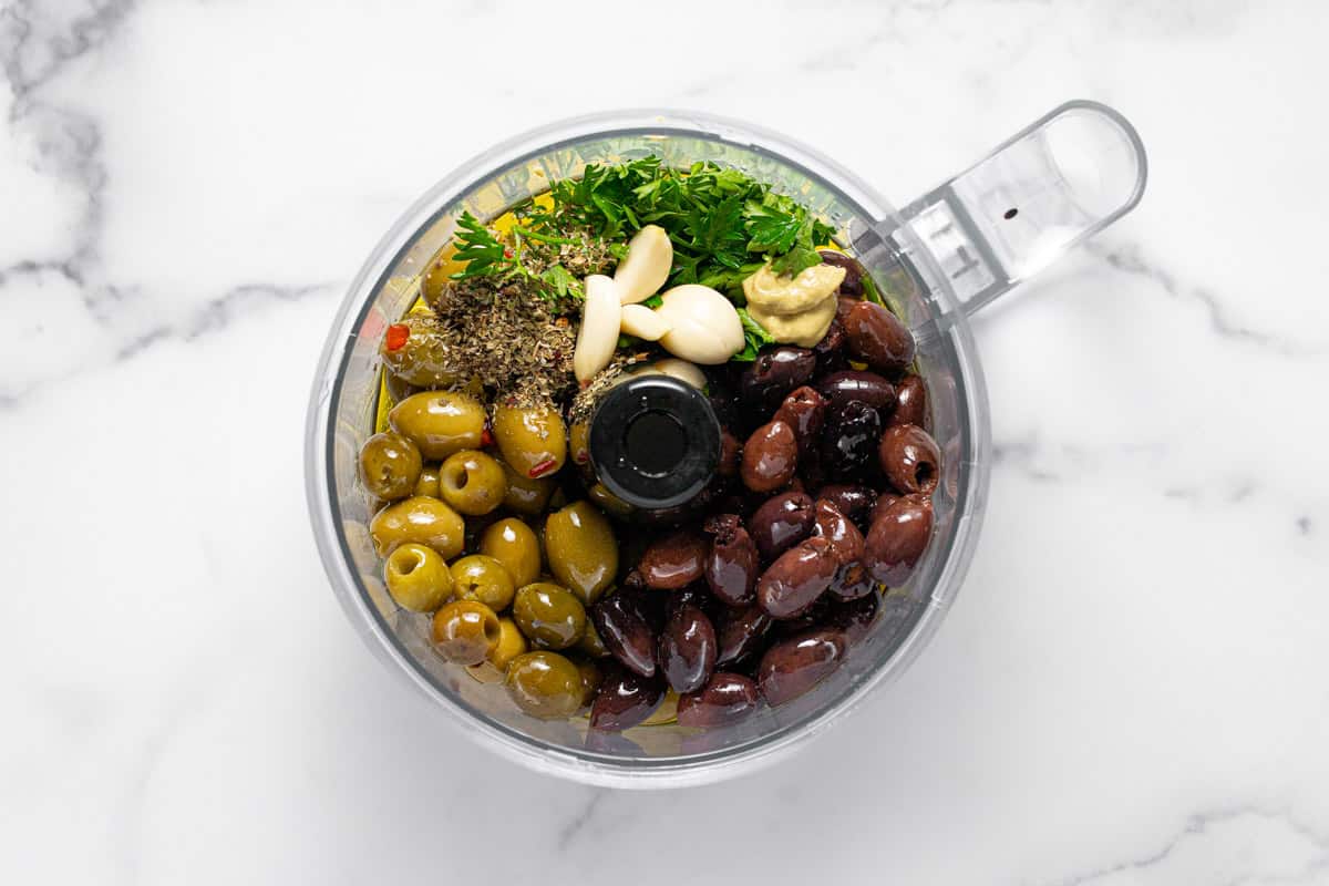Food processor filled with ingredients to make olive tapenade