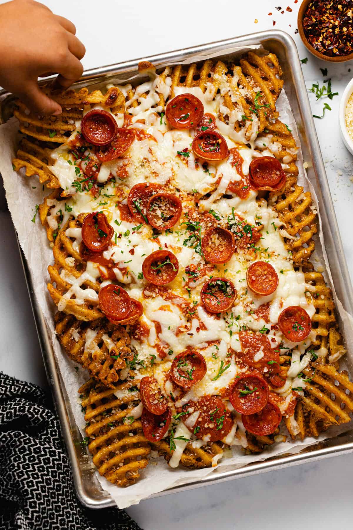 A small baking sheet filled with homemade pizza fries garnished with Parmesan and parsley