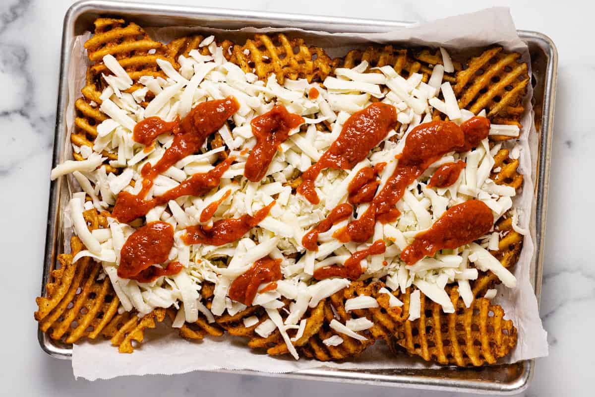 Small parchment-lined baking sheet with ingredients to make homemade pizza fries