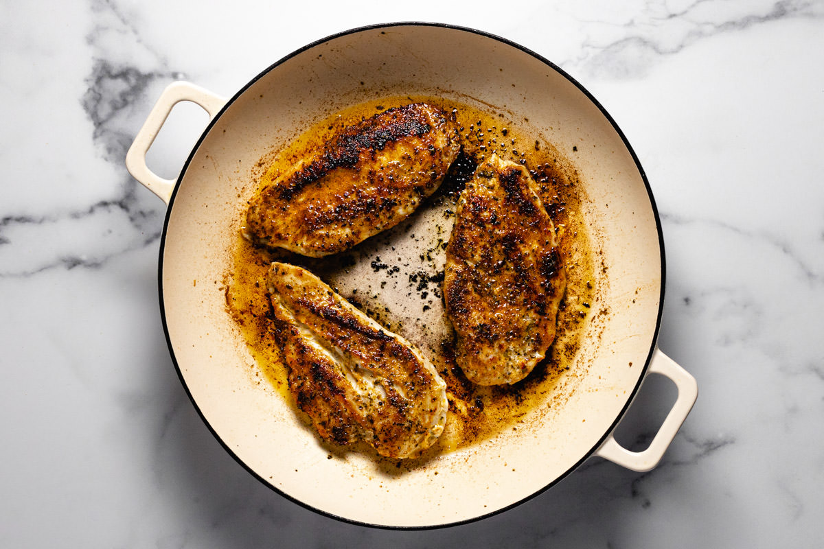 White sauté pan with three cooked chicken breasts in it