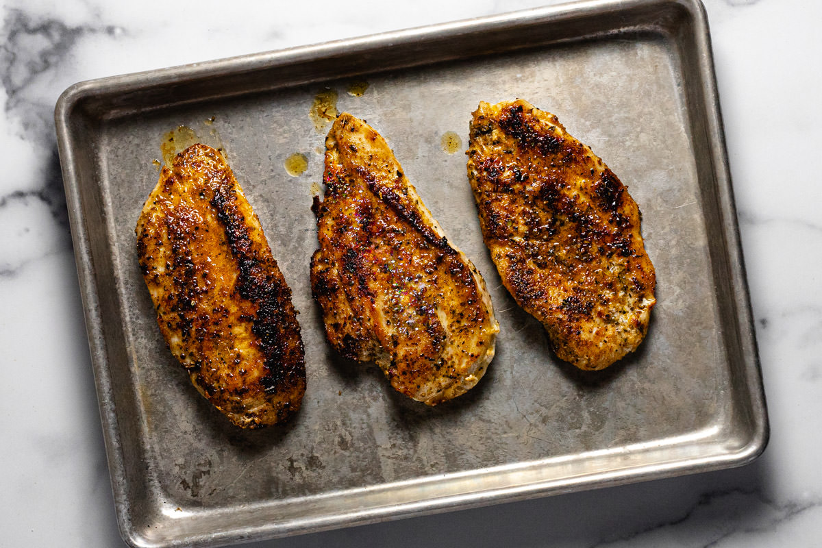 Metal baking sheet with three cooked chicken breasts on it