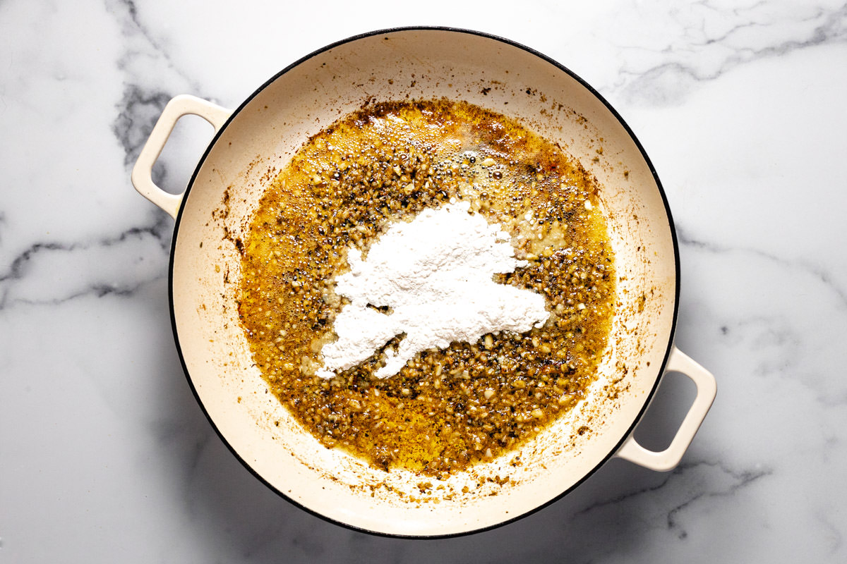 White sauté pan with garlic herbs and all purpose flour