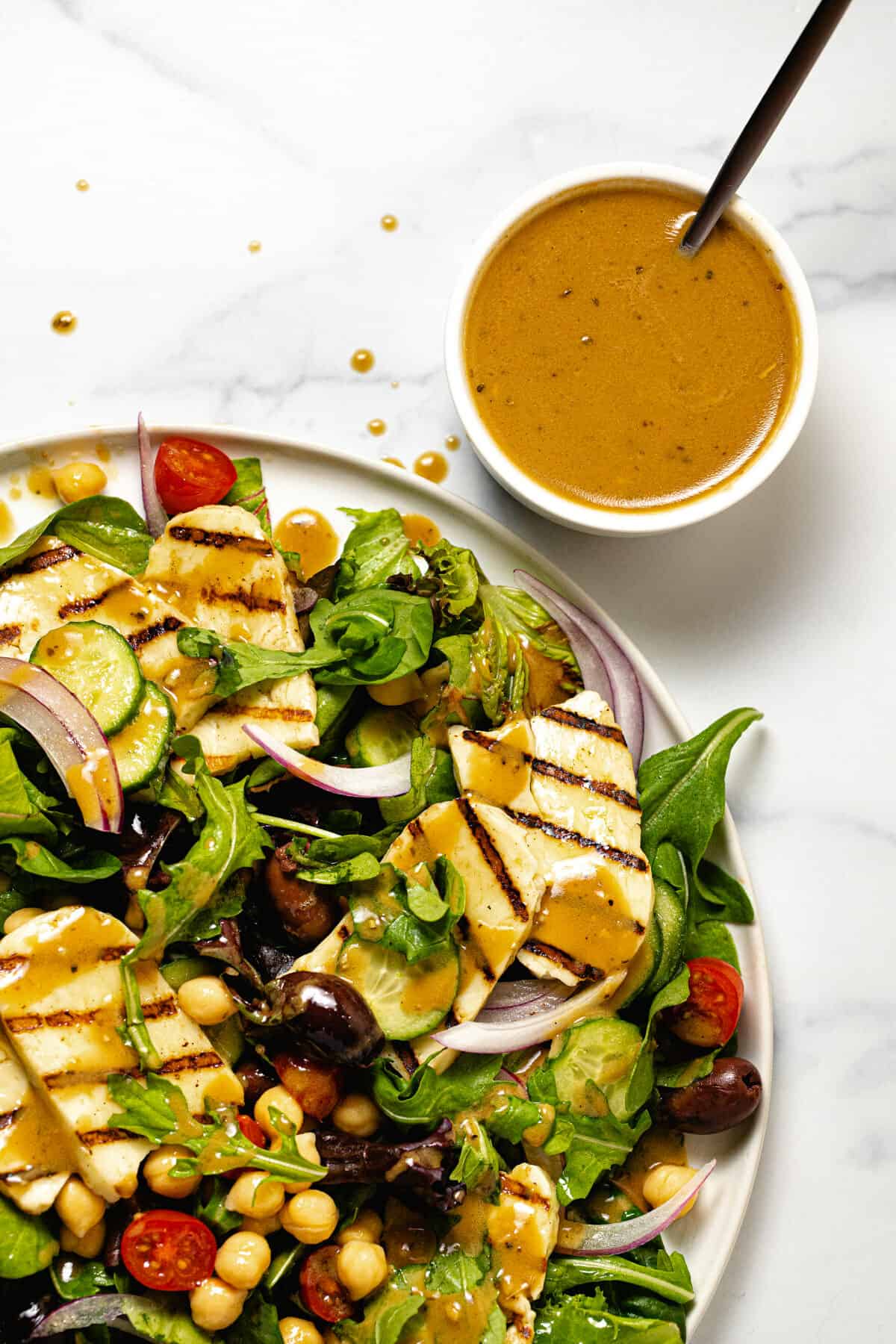 Overhead shot of a bowl of balsamic dressing and a grilled halloumi salad