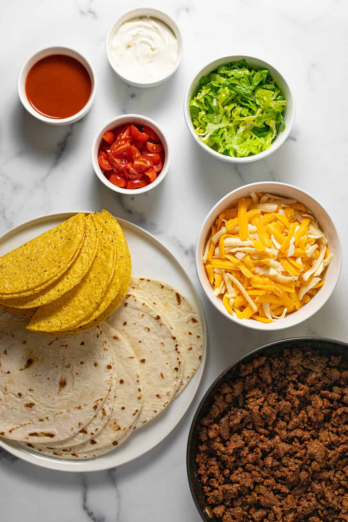 White marble counter top with bowls of ingredients to make cheesy gordita crunch tacos