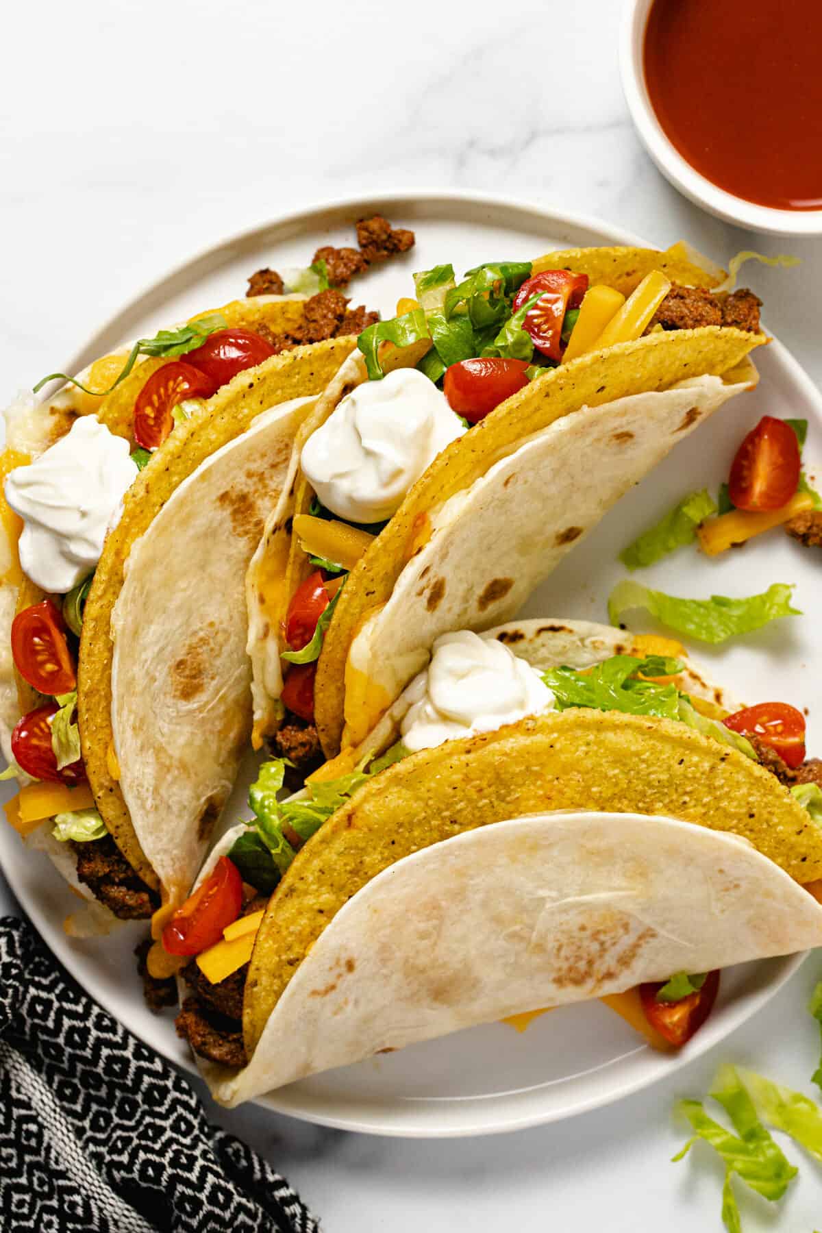 Three cheesy gordita crunch tacos on a white plate topped with sour cream