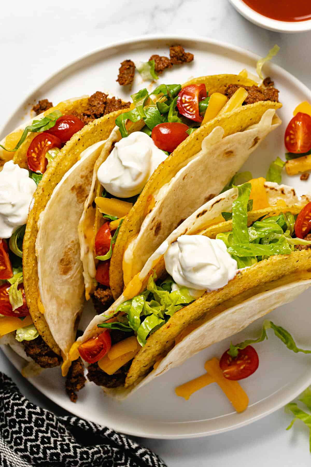Three cheesy gordita crunch tacos on a white plate topped with sour cream