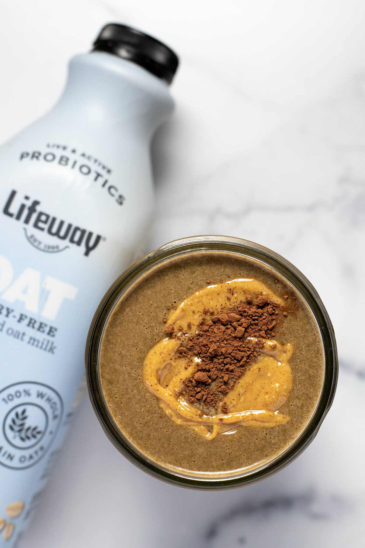 Overhead shot of a chocolate peanut butter smoothie next to a bottle of oat milk