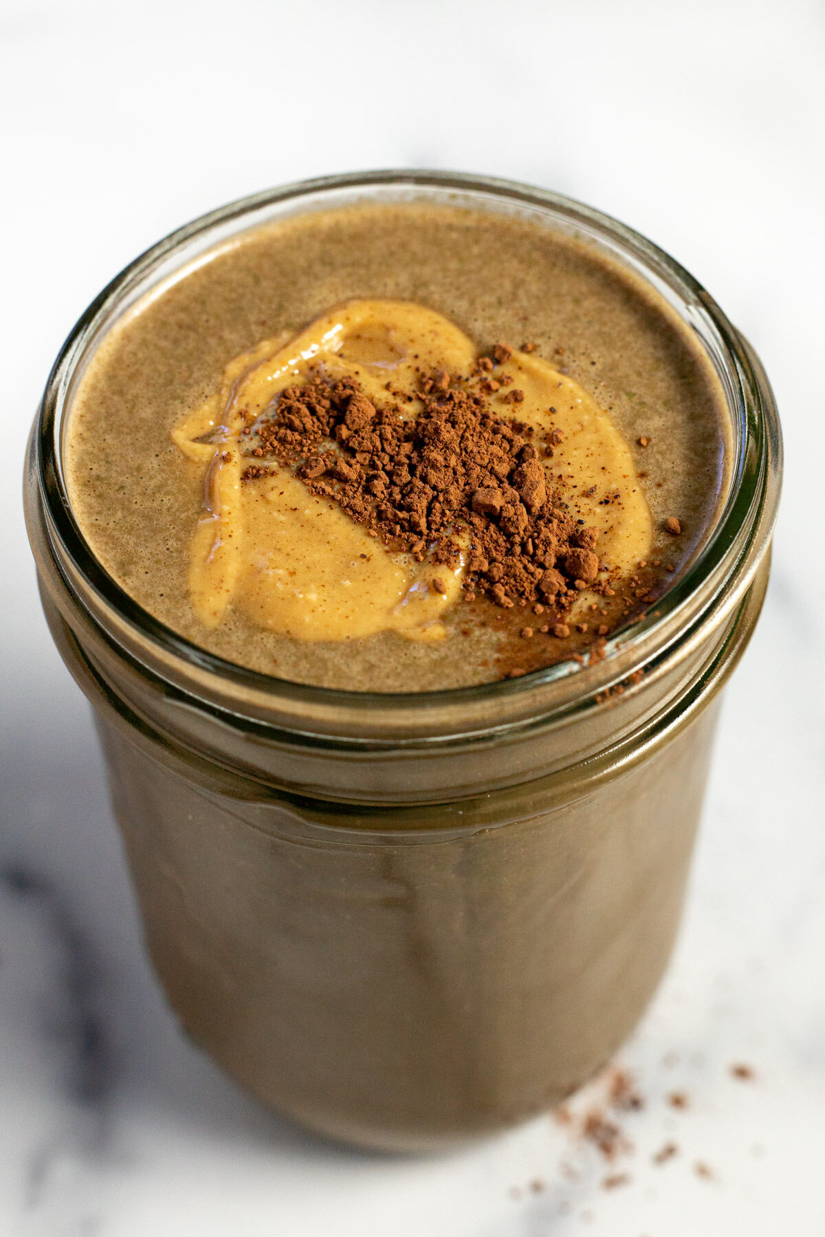 Close up shot of a chocolate smoothie garnished with peanut butter and cocoa powder